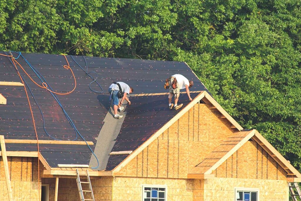 Homeowner examining roof shingles and attic insulation while checking for signs of moisture damage.
