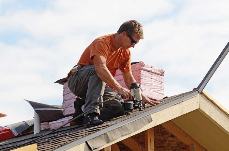 Sunlit asphalt shingles show faded areas and scattered granules beside a roof gutter.